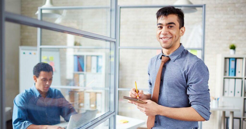 happy male worker in modern office holding pencil and notepad
