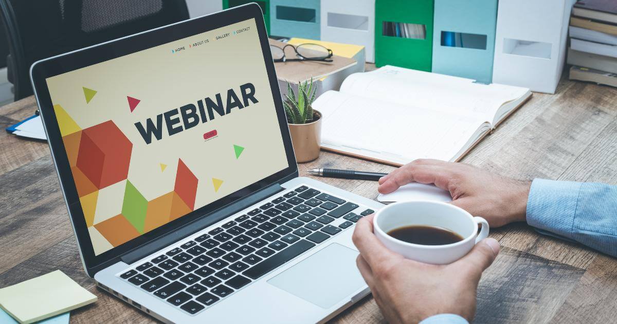worker with cup of coffee looking at laptop with webinar on screen